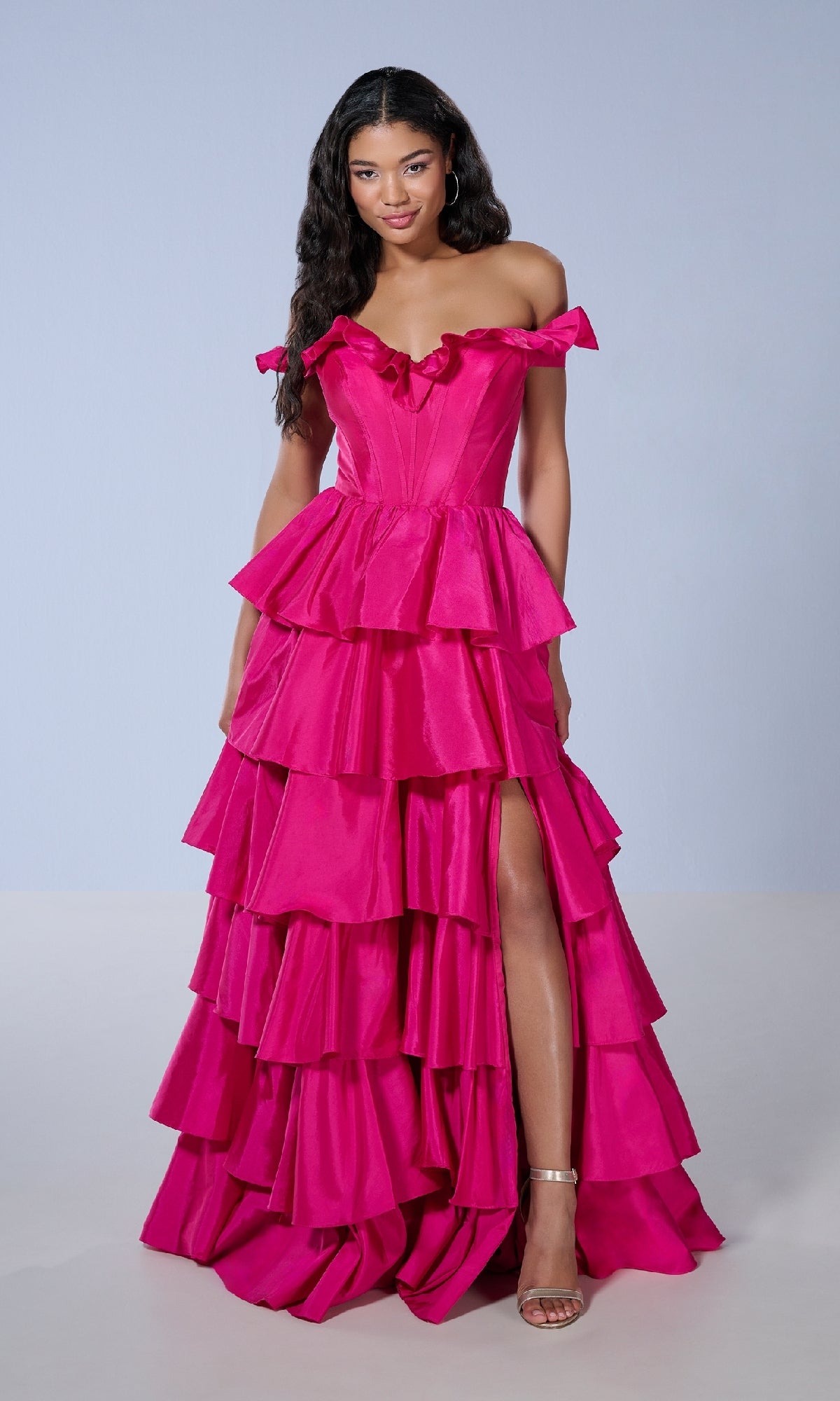 A woman models the Tiffany 16175 long prom dress—bright pink, off-the-shoulder with a corset bodice, tiered ruffle skirt, thigh-high slit—and strappy heels against a plain light background.